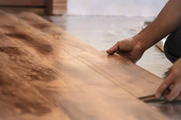 Hands installing hardwood floor planks.