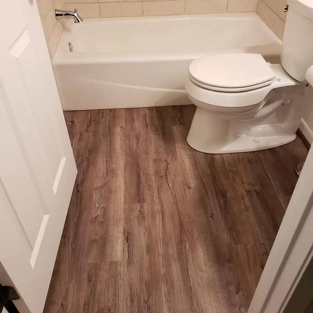 Minimalist bathroom with a white bathtub, tiled walls, and wood-style vinyl flooring.