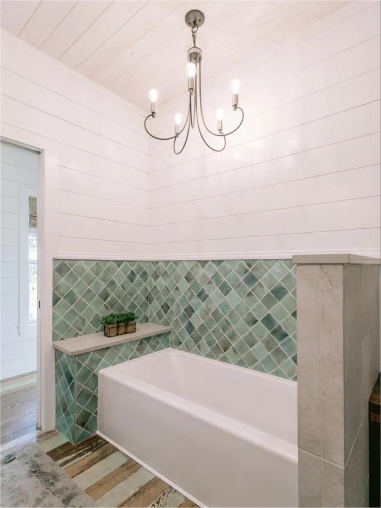 Rustic bathroom with green diamond-shaped tile backsplash and chandelier.